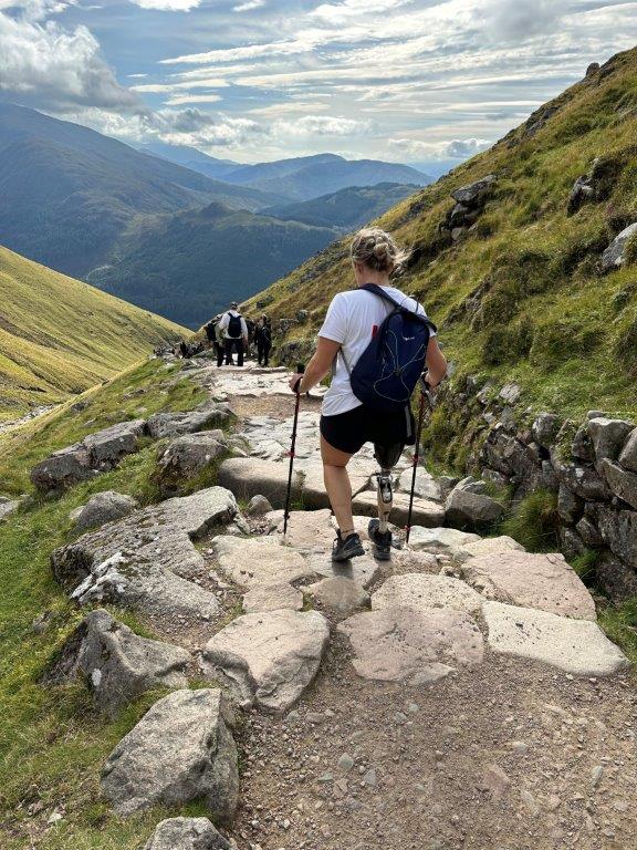 Lianne, an amputee, walking down Ben Nevis with a beautiful scenery infront of her.